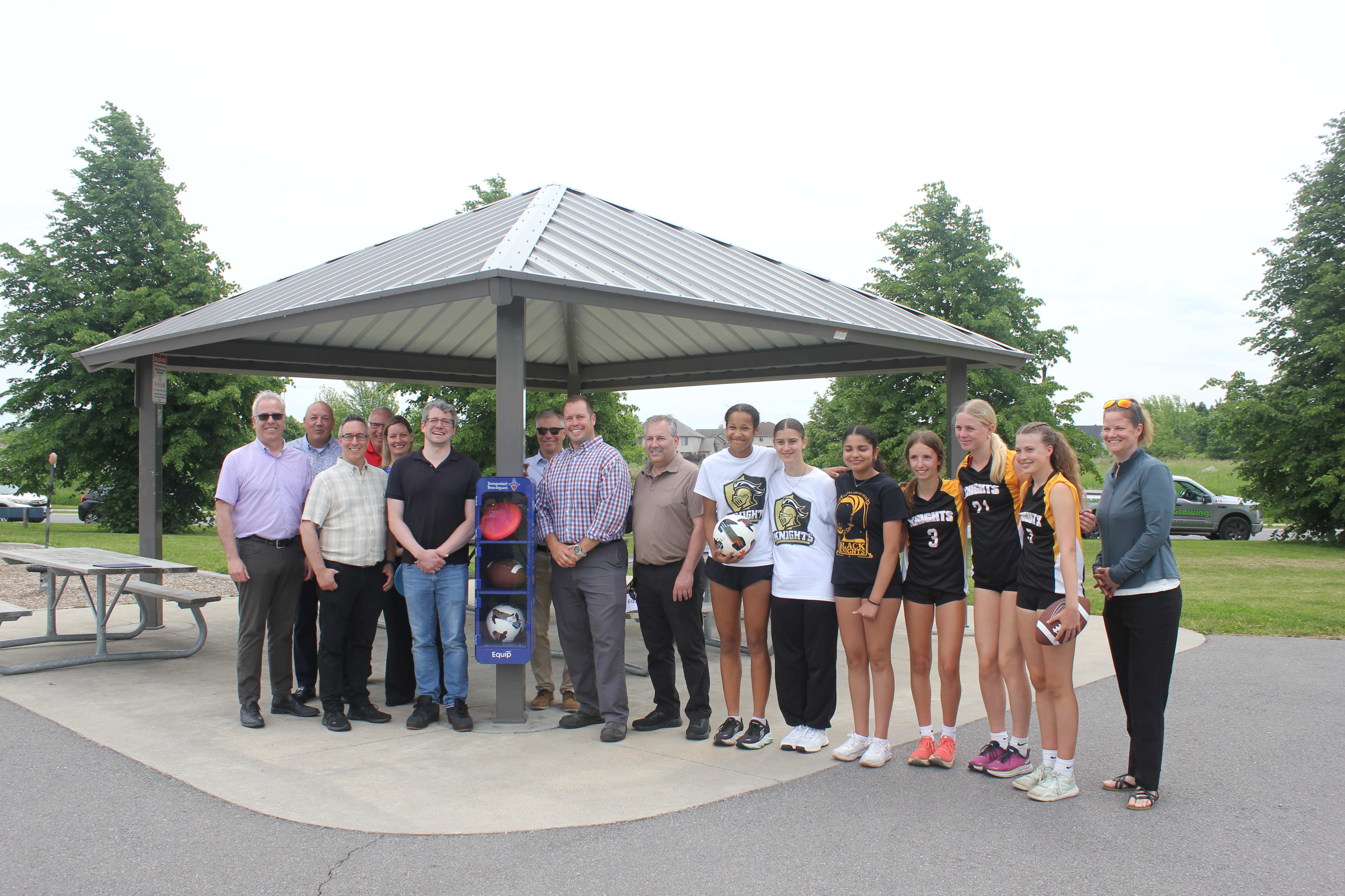 Members of city council, city staff and community members pose for a photos in front of a self-serve sport equipment locker at Molly McGlynn Park.