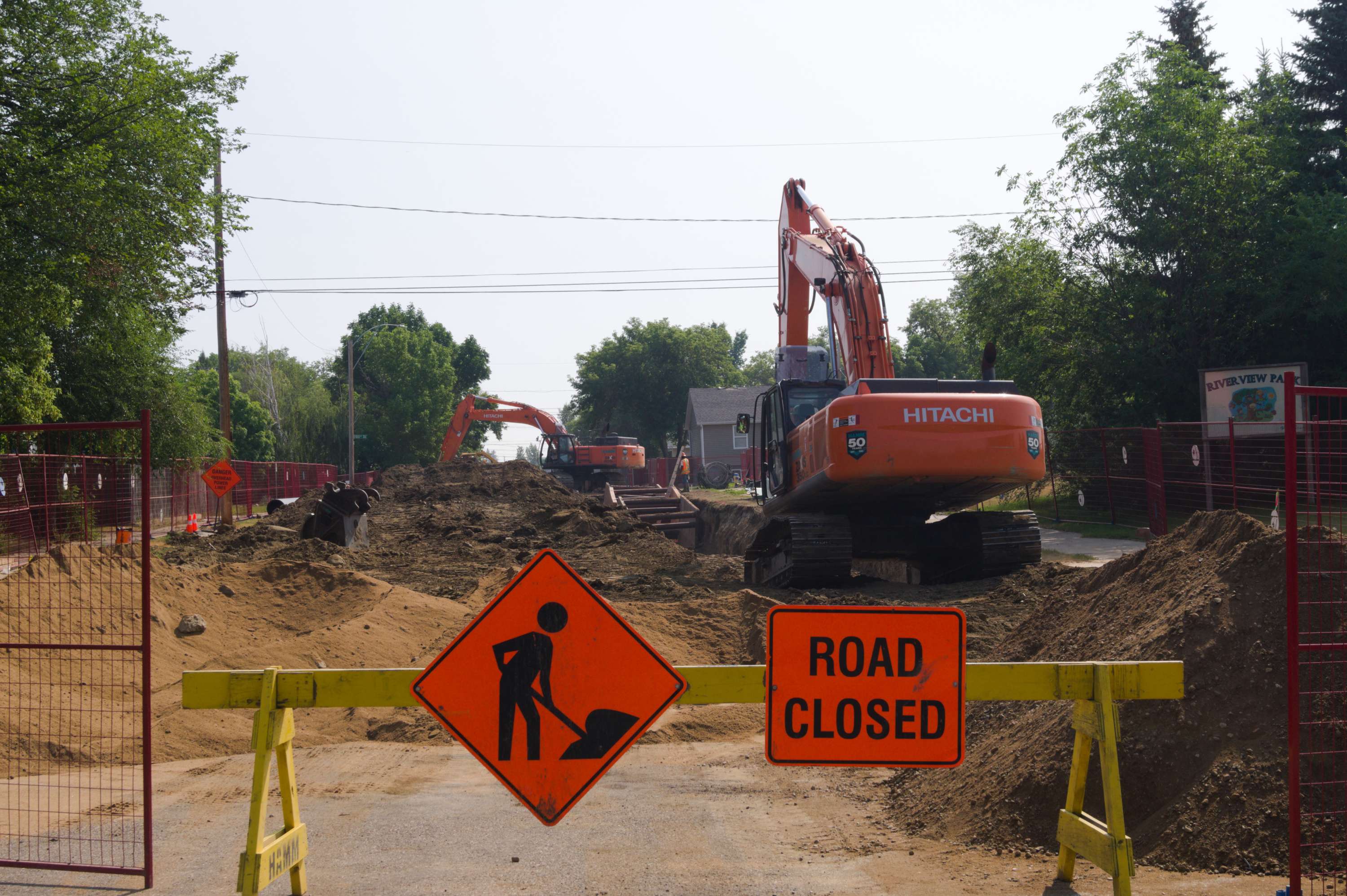 A road closed sign in front of heavy machinery digging up the pavement