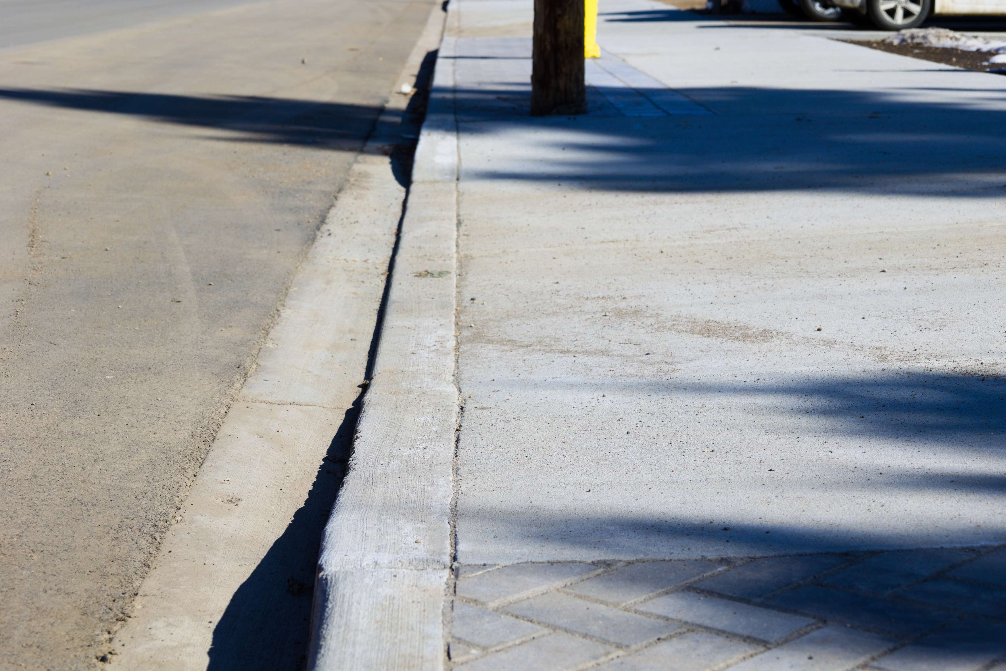 Concrete curb and sidewalk along a residential street with patterned paving details.