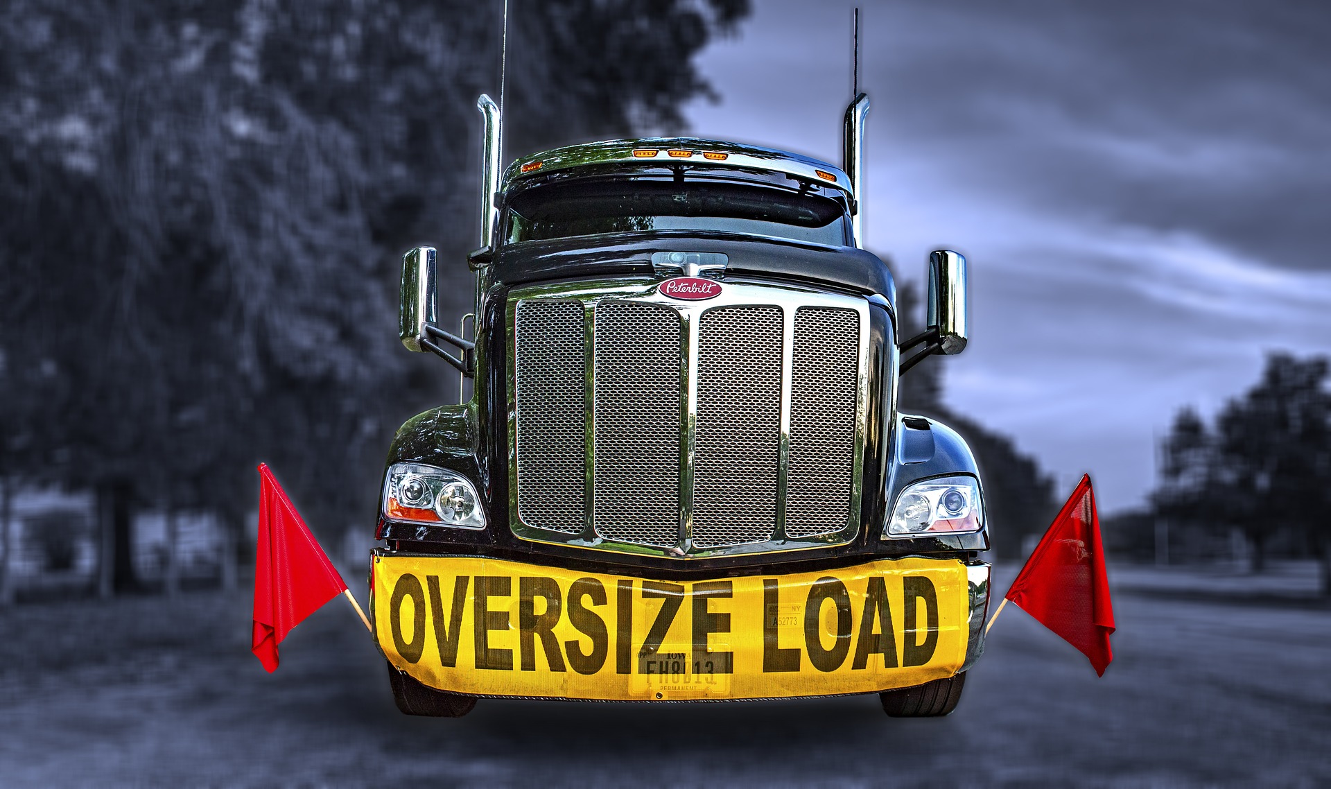 Large black truck with "OVERSIZE LOAD" sign and warning flags on either side.