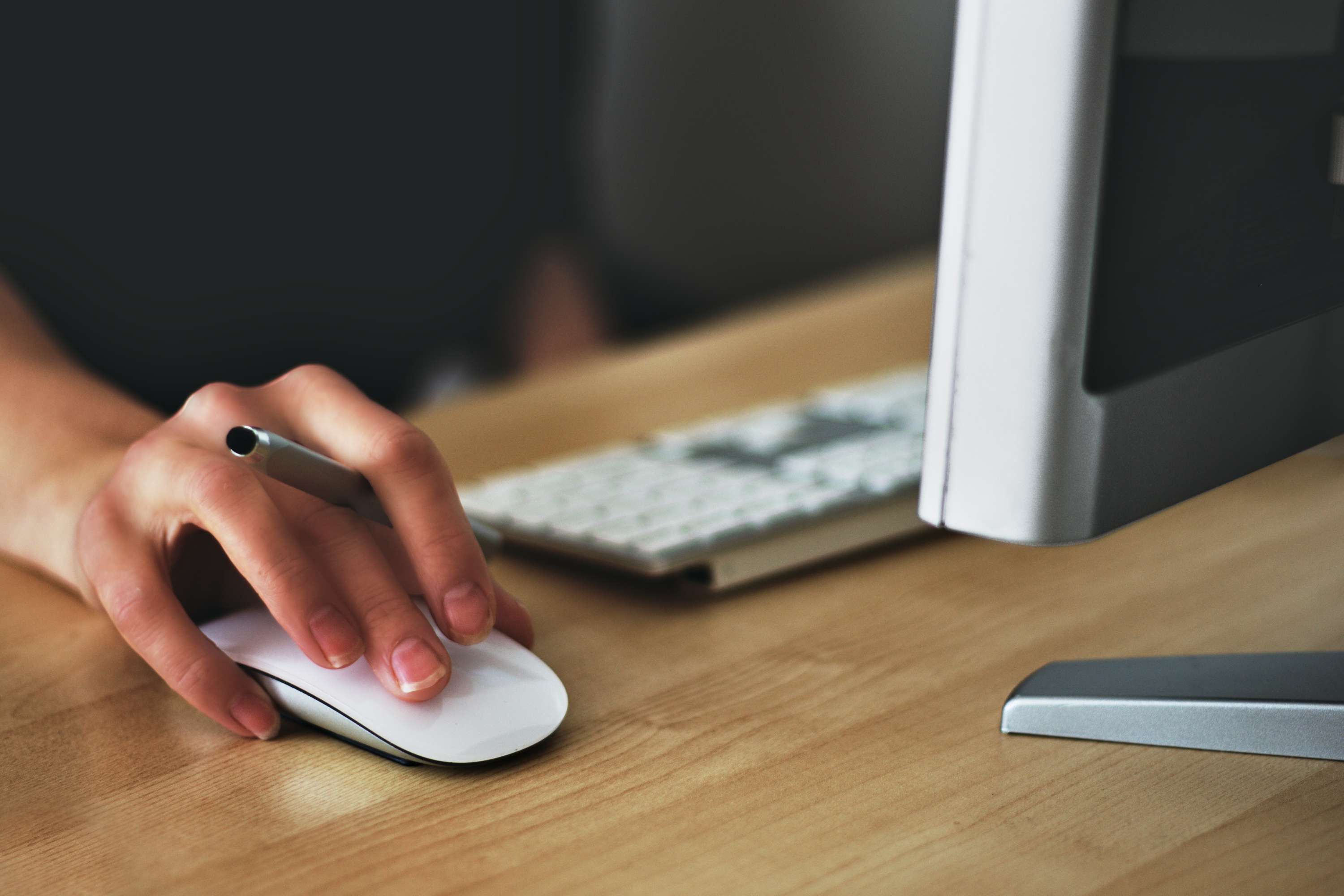 Hand using a computer mouse beside a keyboard and monitor on a desk.