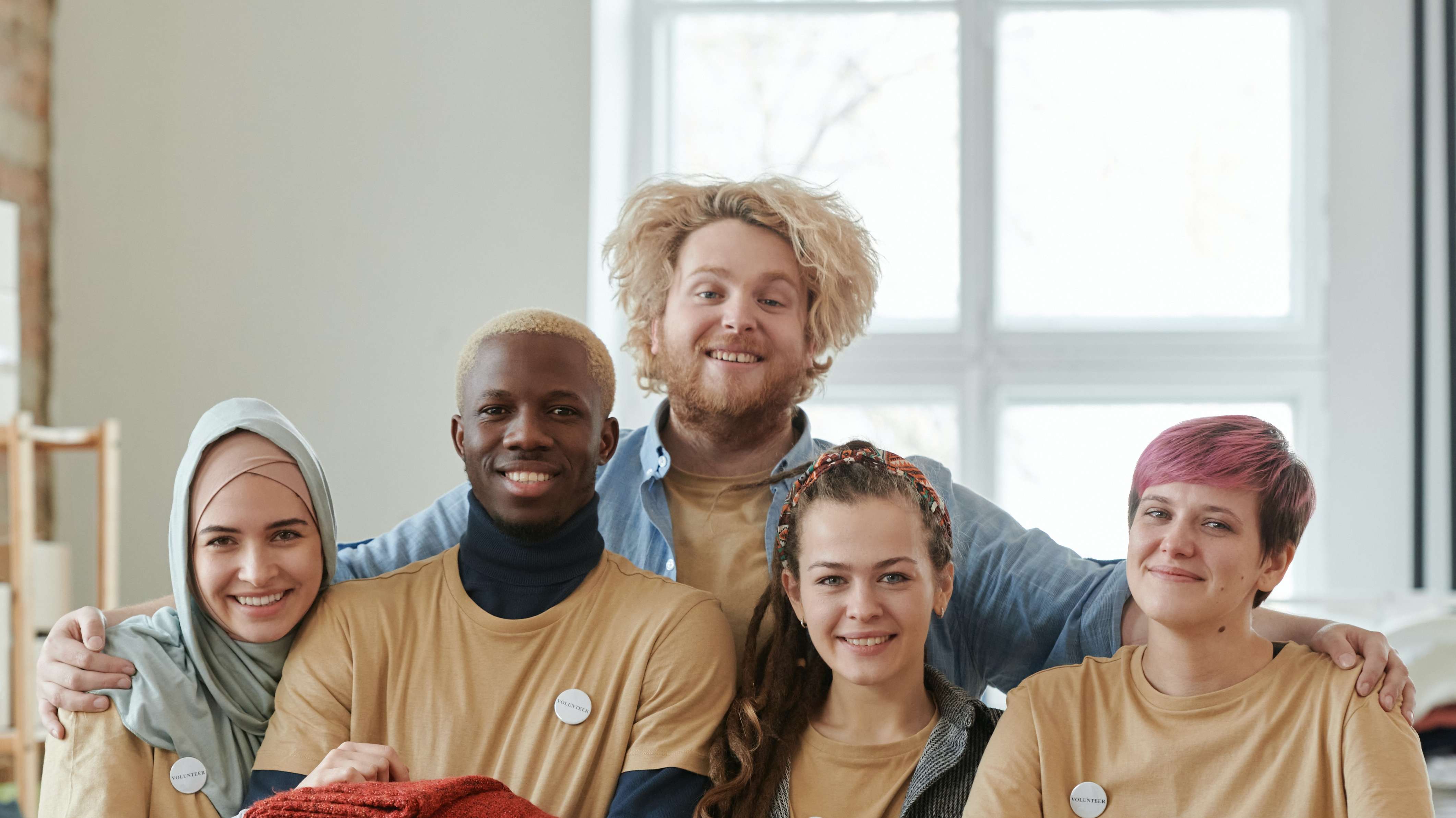 Group of young volunteers smiling together, wearing matching shirts and badges in a bright space.