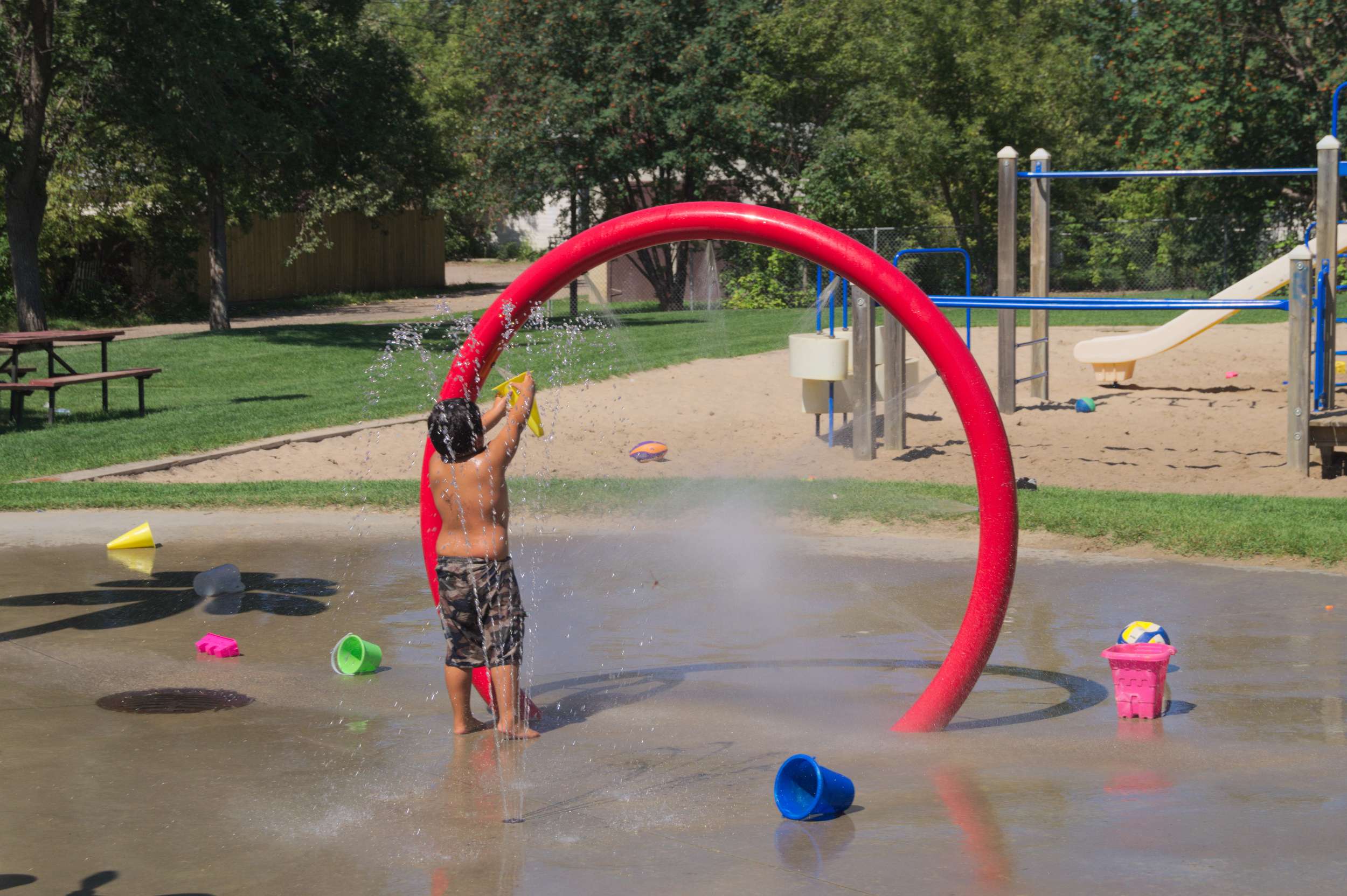 Child playing with water in a splash park under a red circular sprinkler ring.