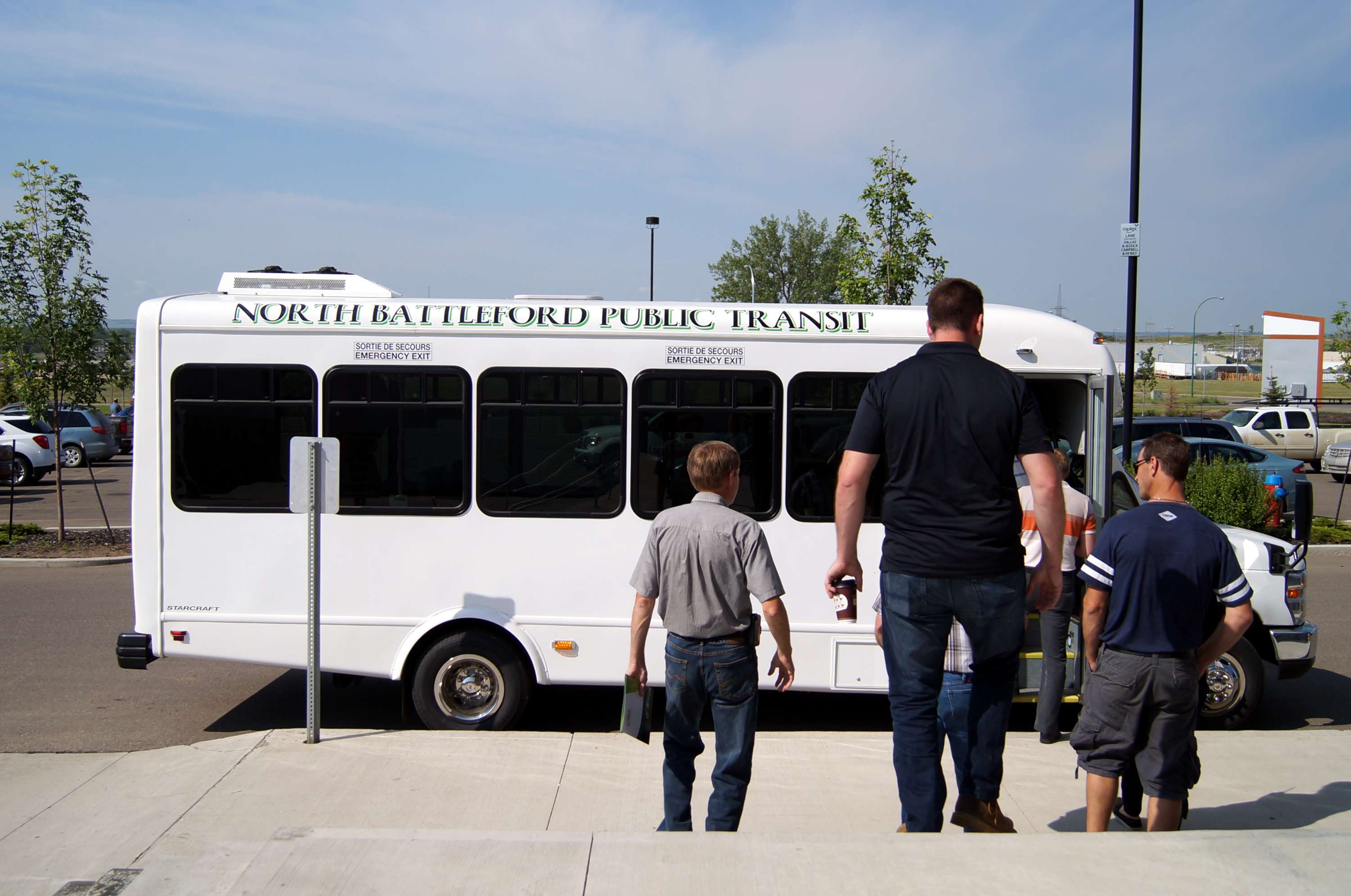People walking toward a North Battleford Public Transit bus at a transit stop.