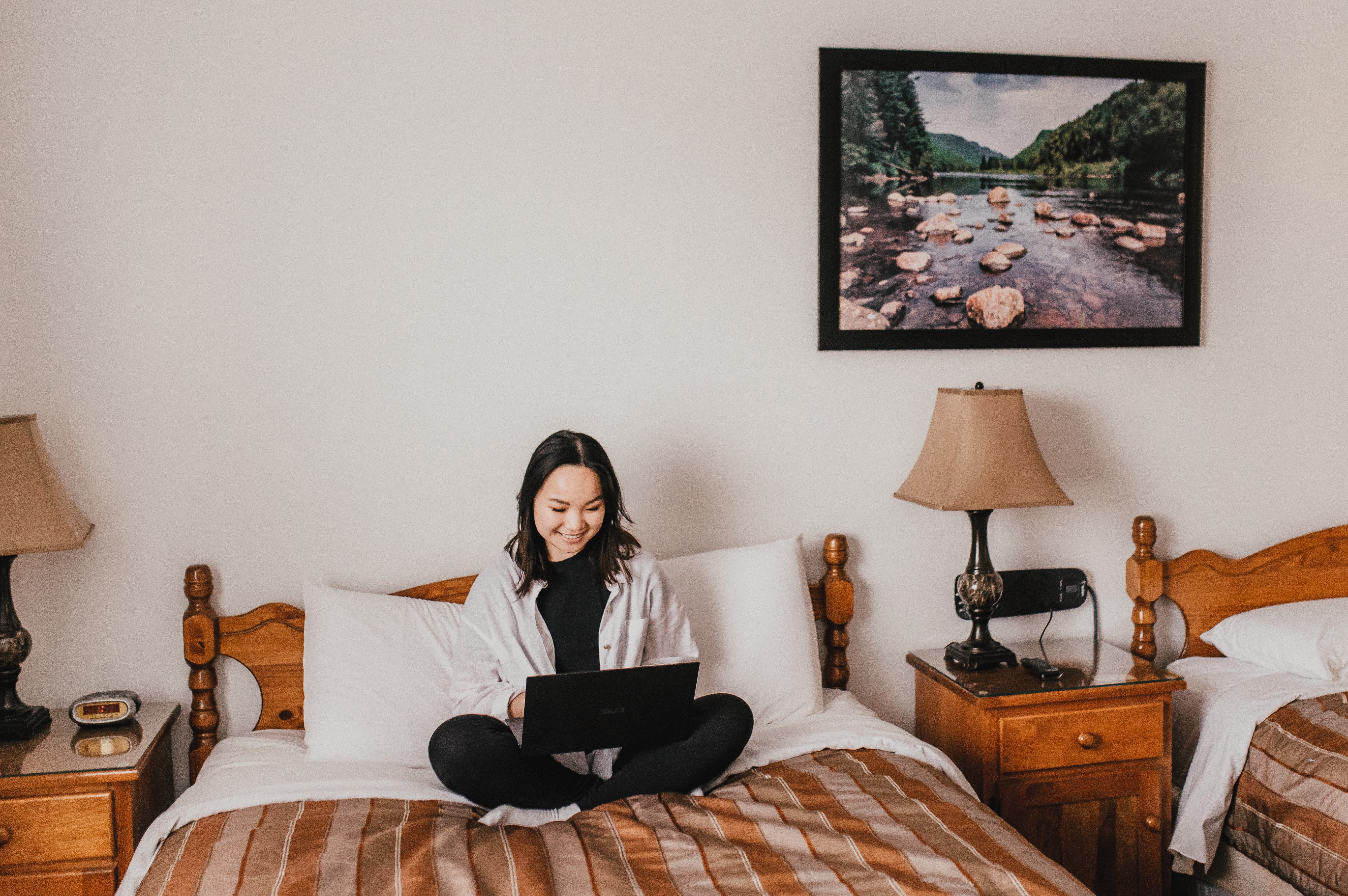 A woman sits on a motel bed working on her computer