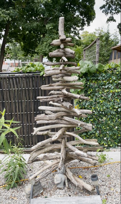 A crafted tree made from driftwood pieces sits outside in a yard