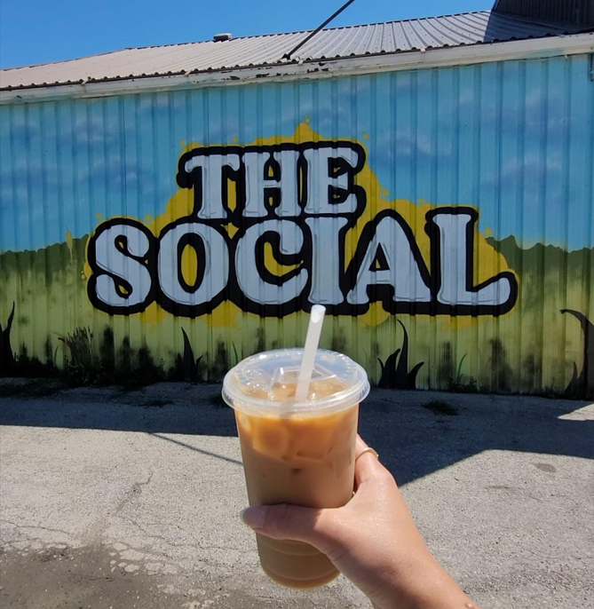 Someone holding an iced coffee in front of a sign that says "the social"