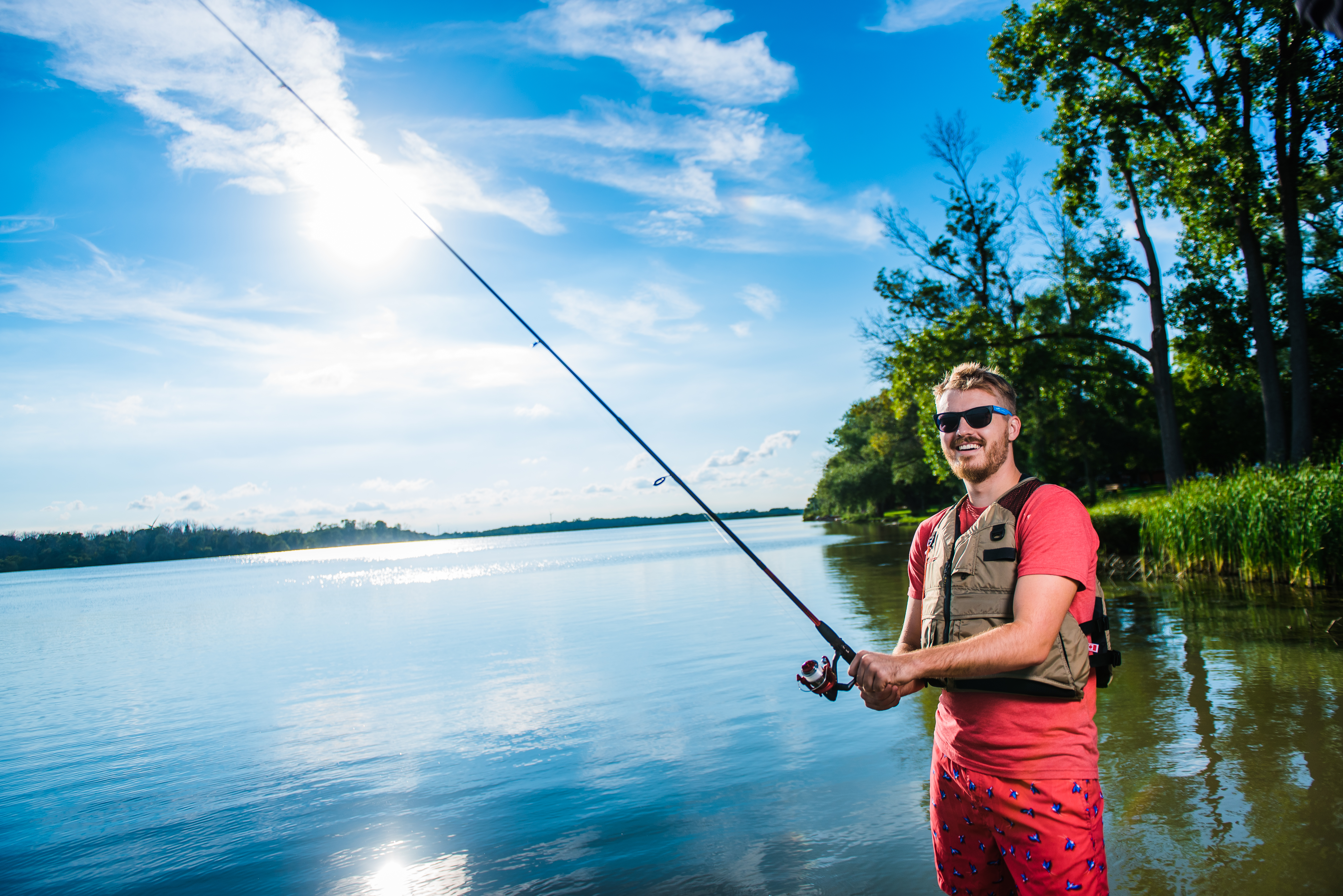 man standing holding a fishing rod by the water 