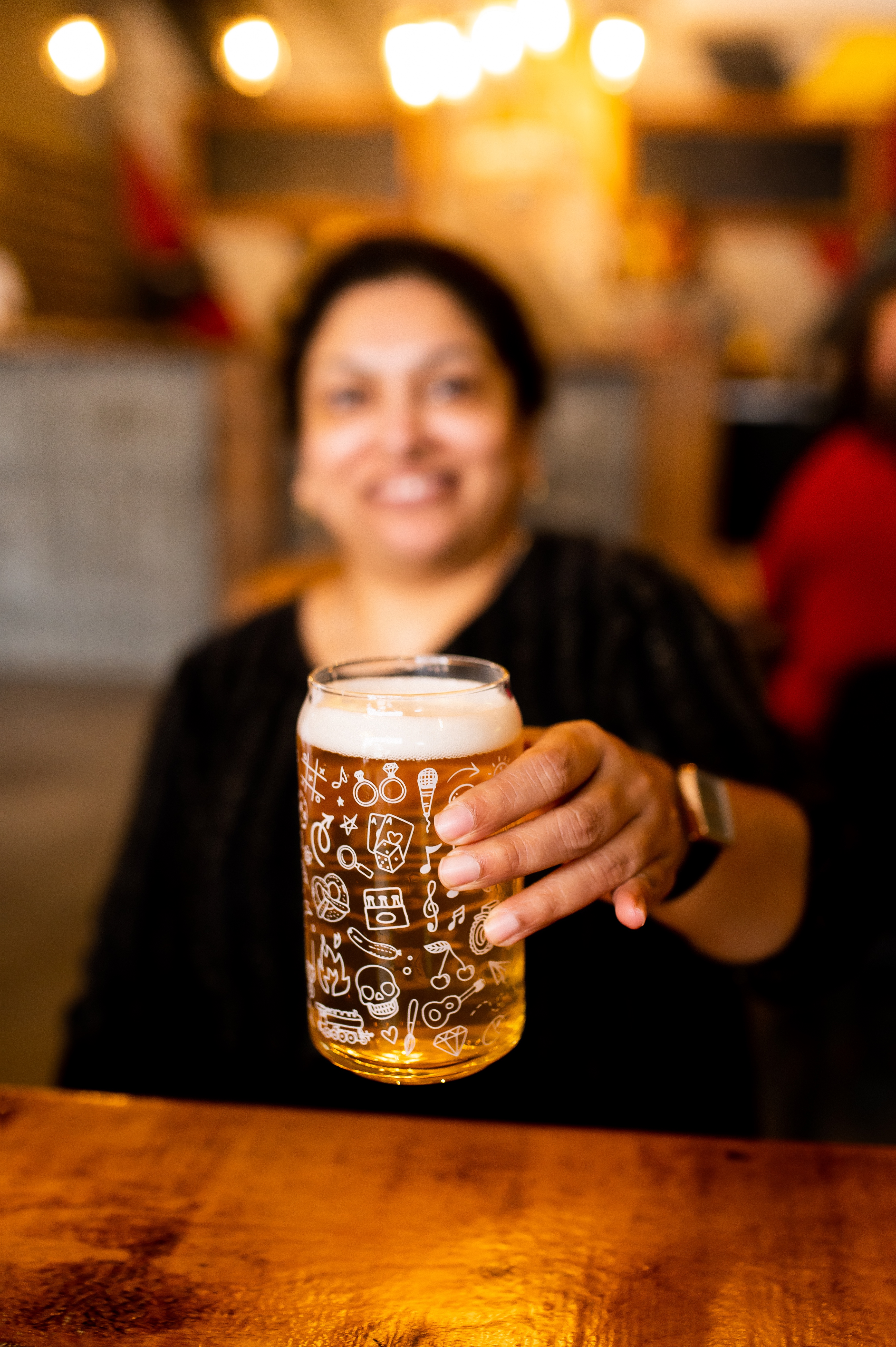 a woman holds up a cold beer in a clear glass with white images etched into the glass