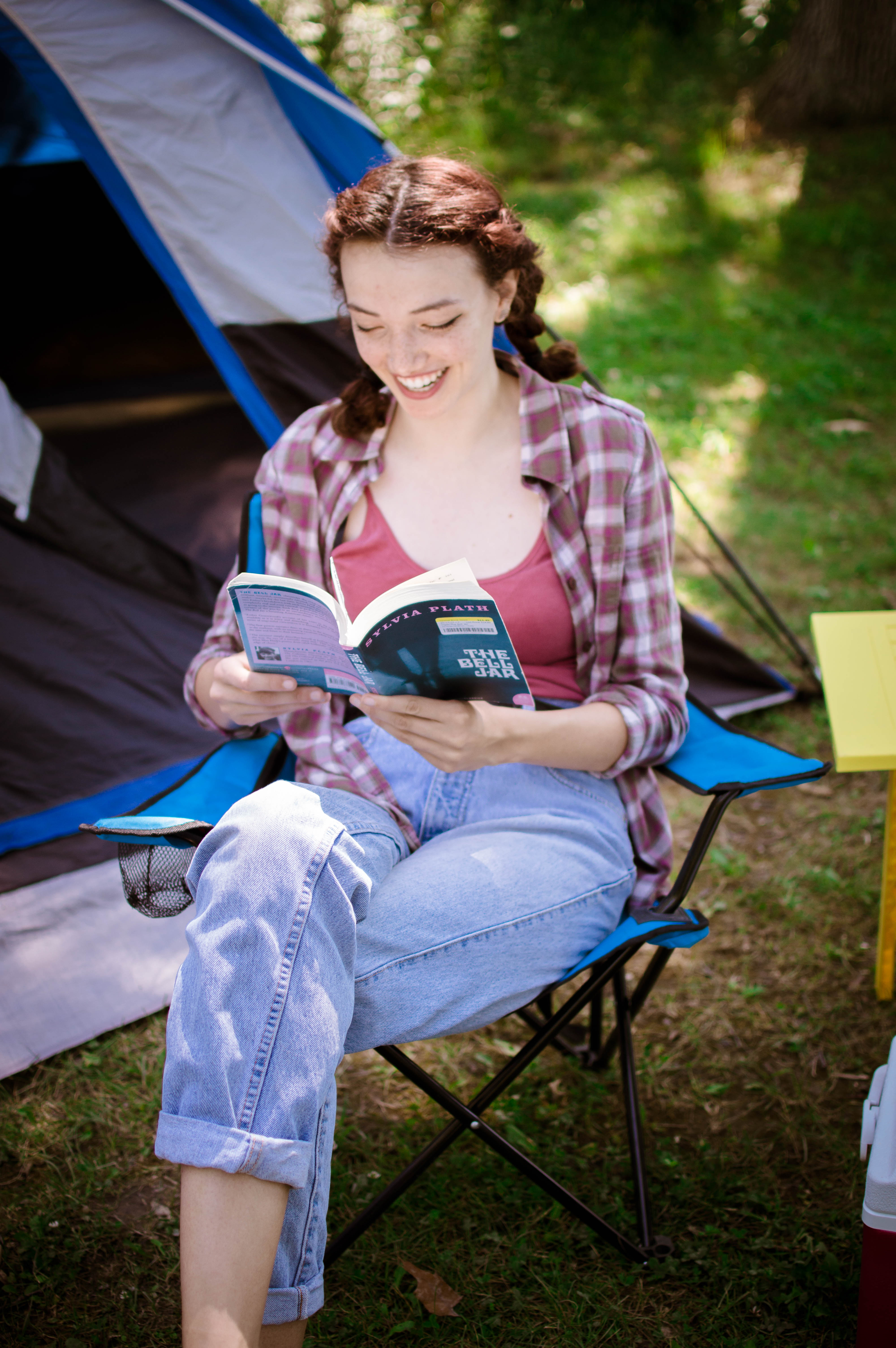 A woman sits in a lawn chair reading a book in front of a blue tent