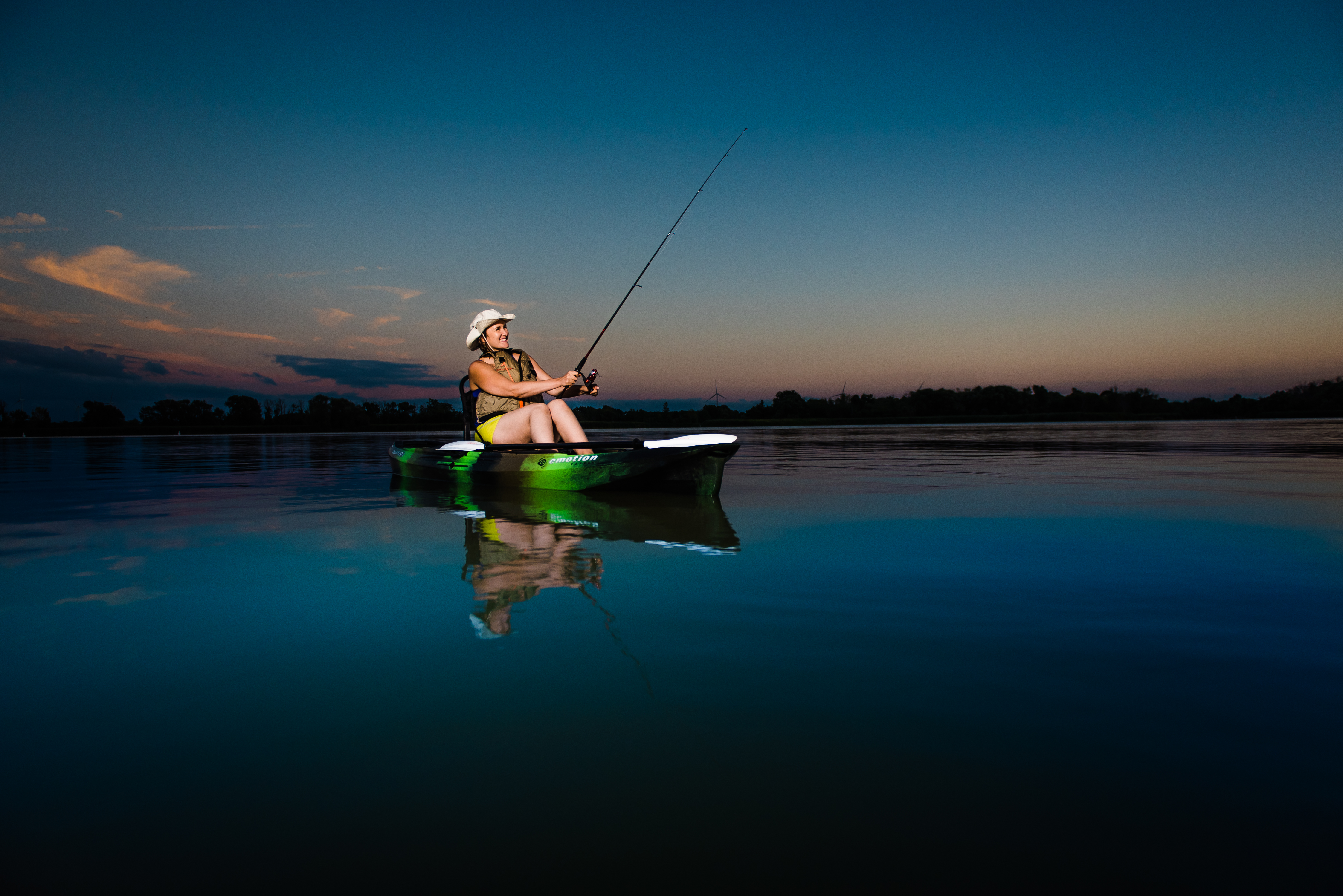 A woman fishing in a kayak at sunset