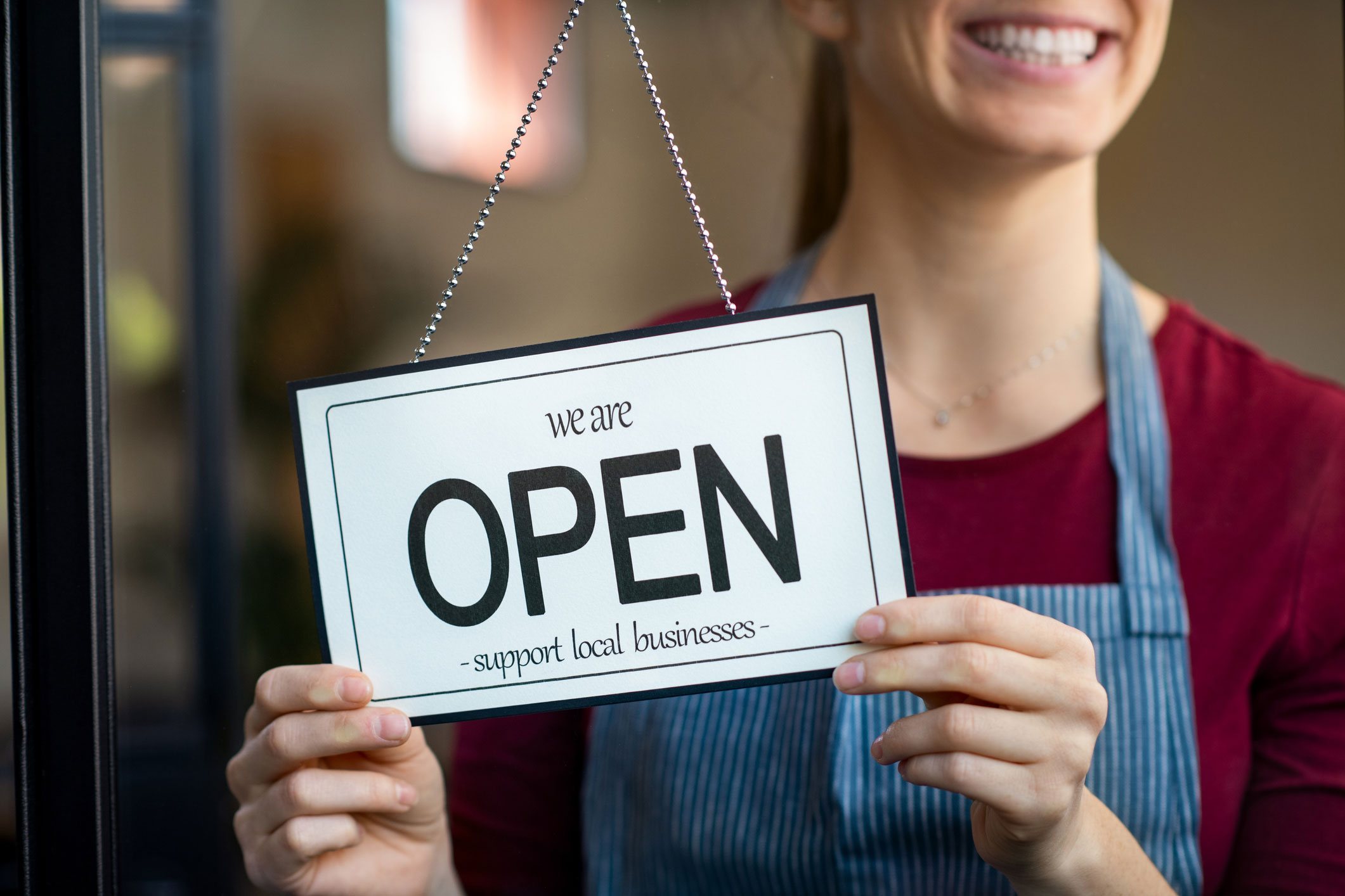 Woman holding 'Open - support local business' sign on the inside door.