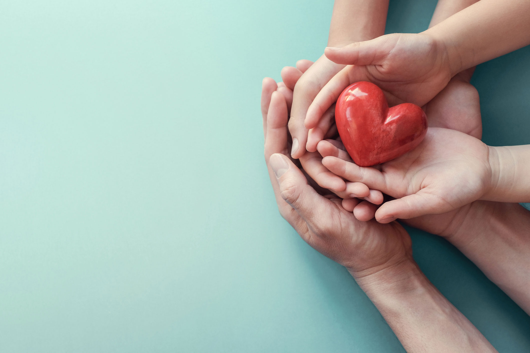 Adult and child hands holding red heart on aqua background concept for health