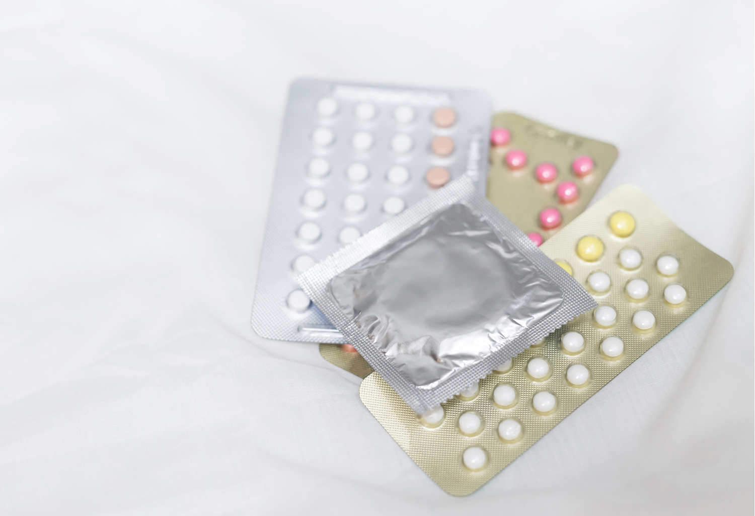 Three packs of birth control pills with a condom in a wrapper sitting on top. 