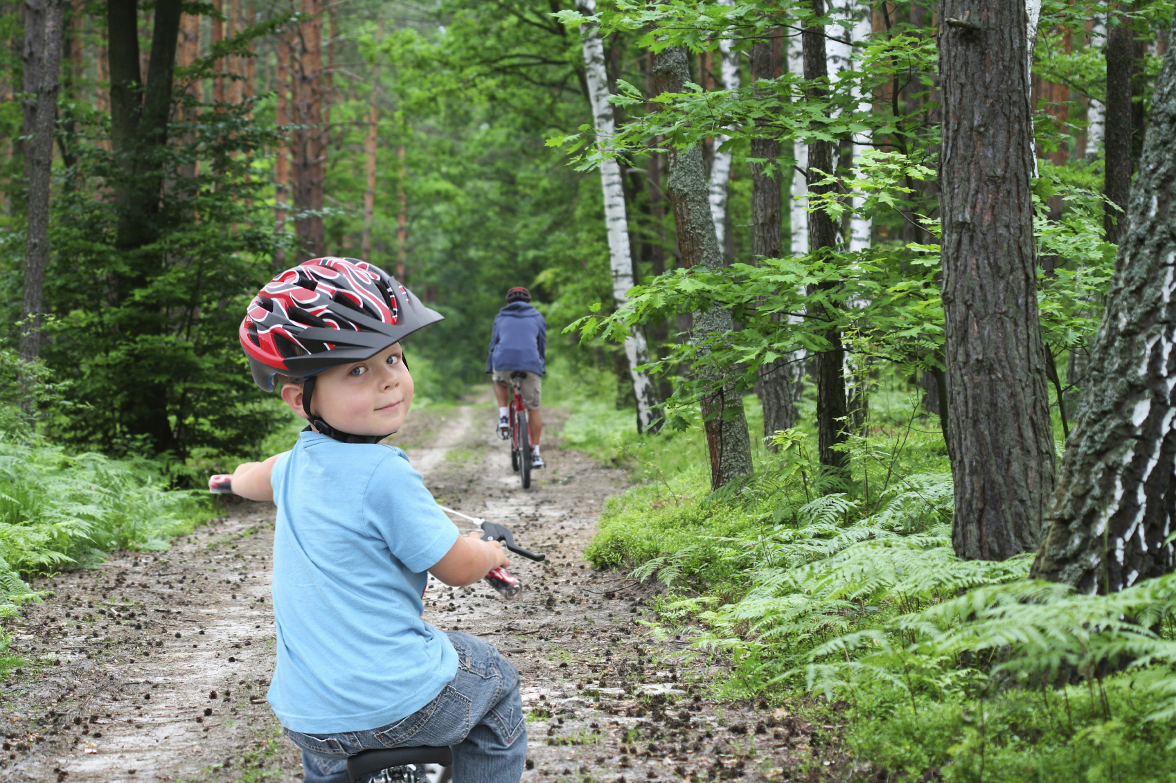 boy riding bicycle on trail wearing a helmet looking back over his shoulder