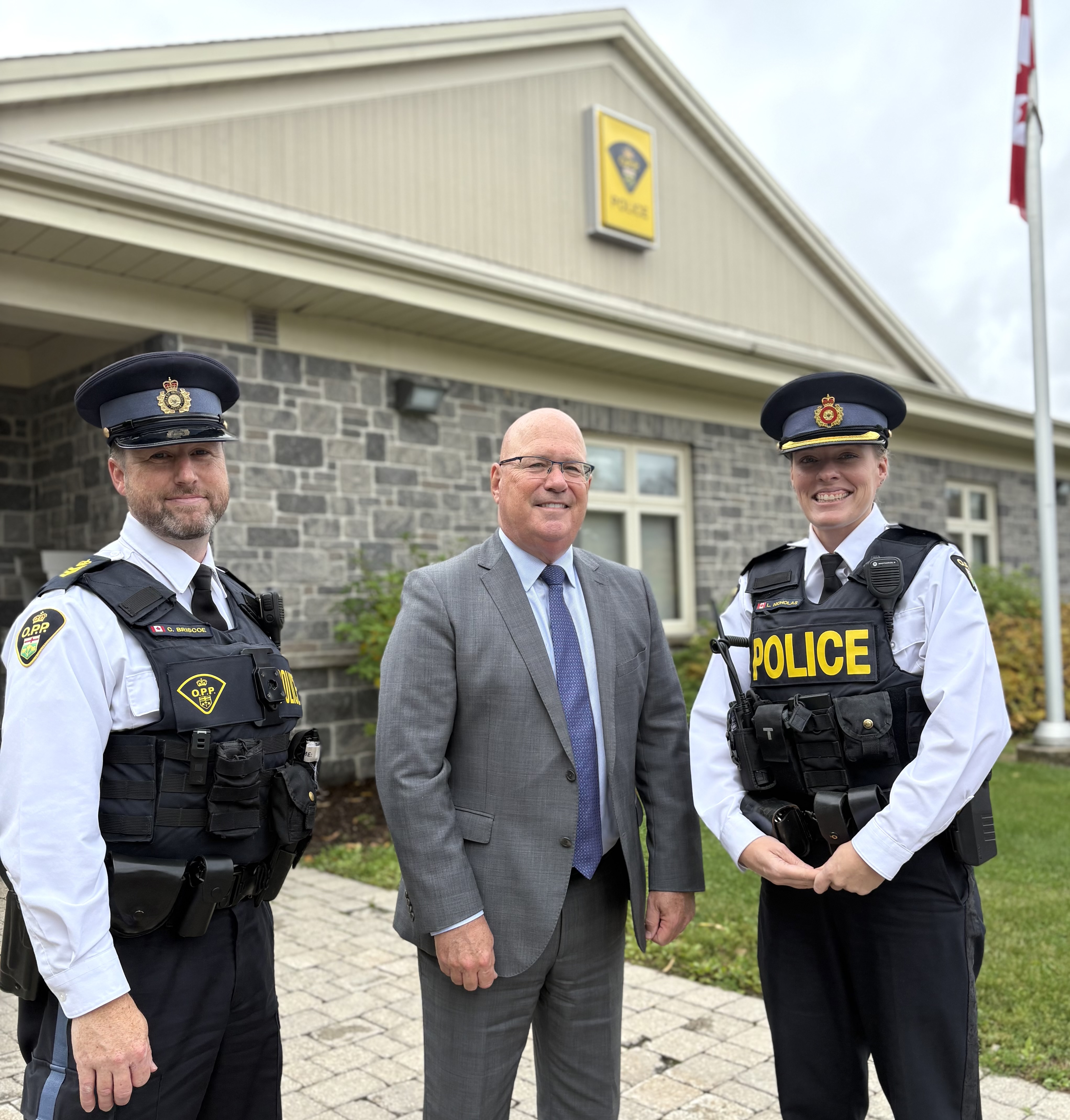 Two Police Officers and MPP Clark standing in front of an OPP station