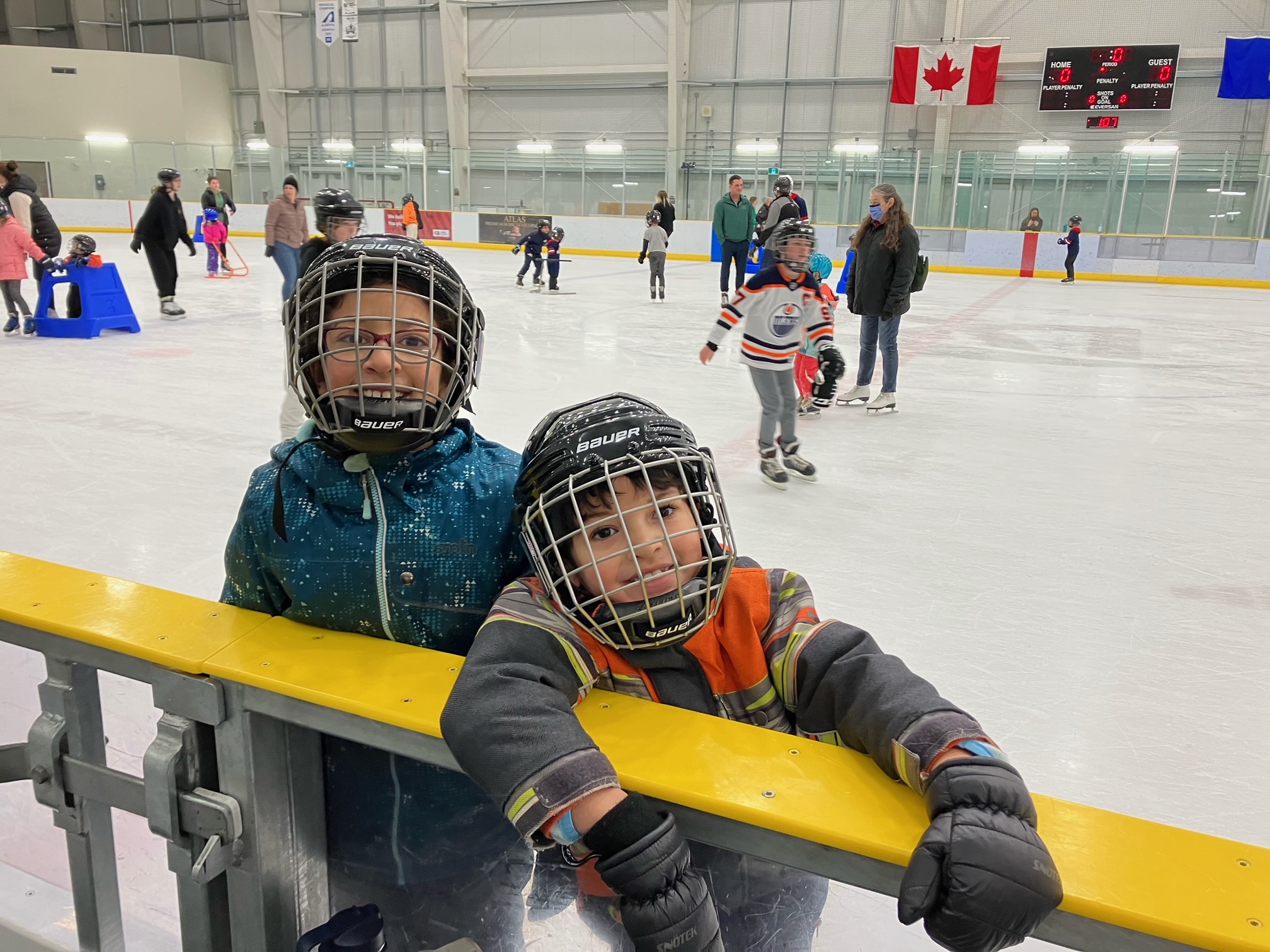 children smiling haning over the ledge of the indoor ice rink