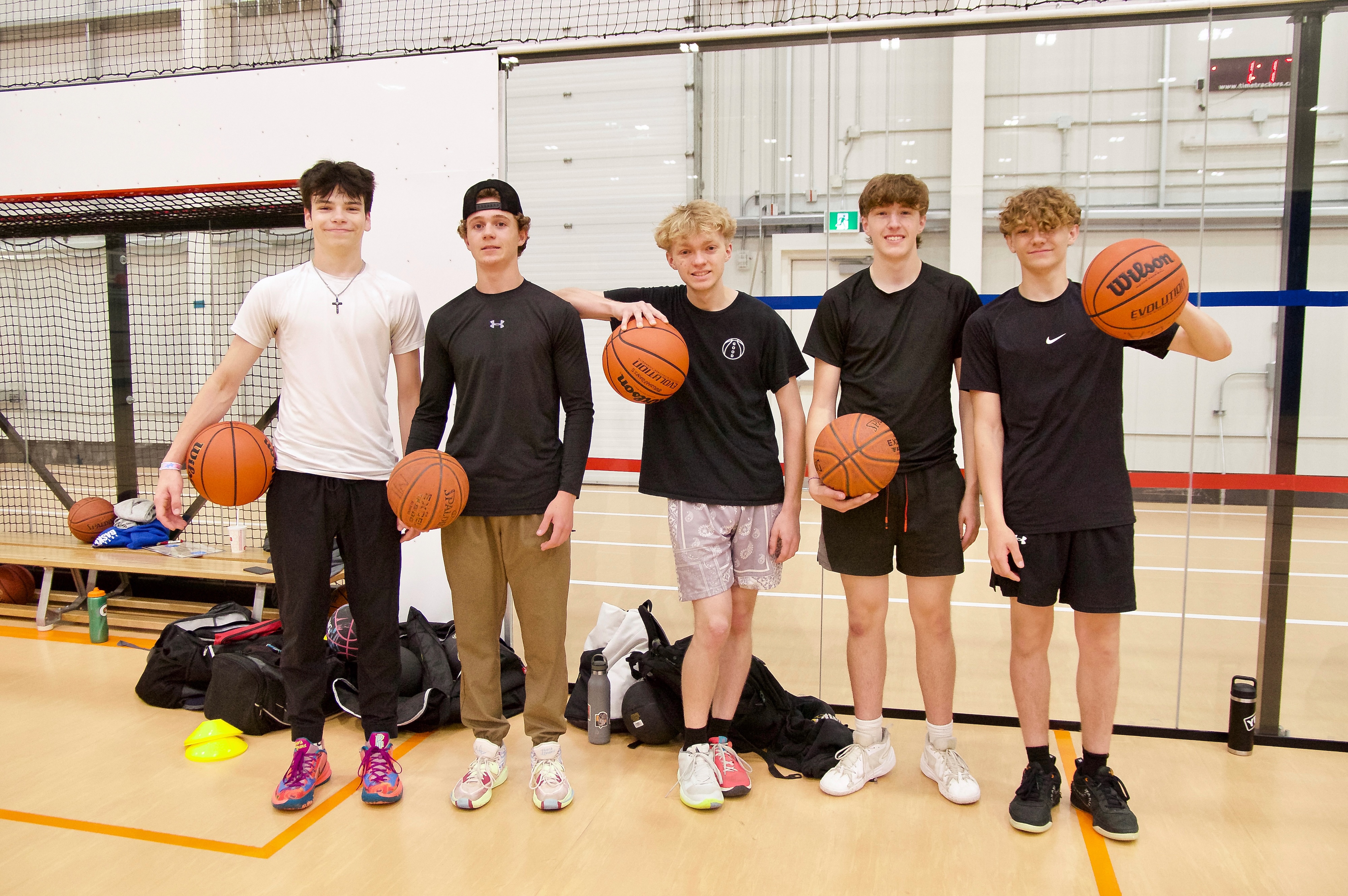 a group of friends holding up their basketballs standing on a basketball court indoors