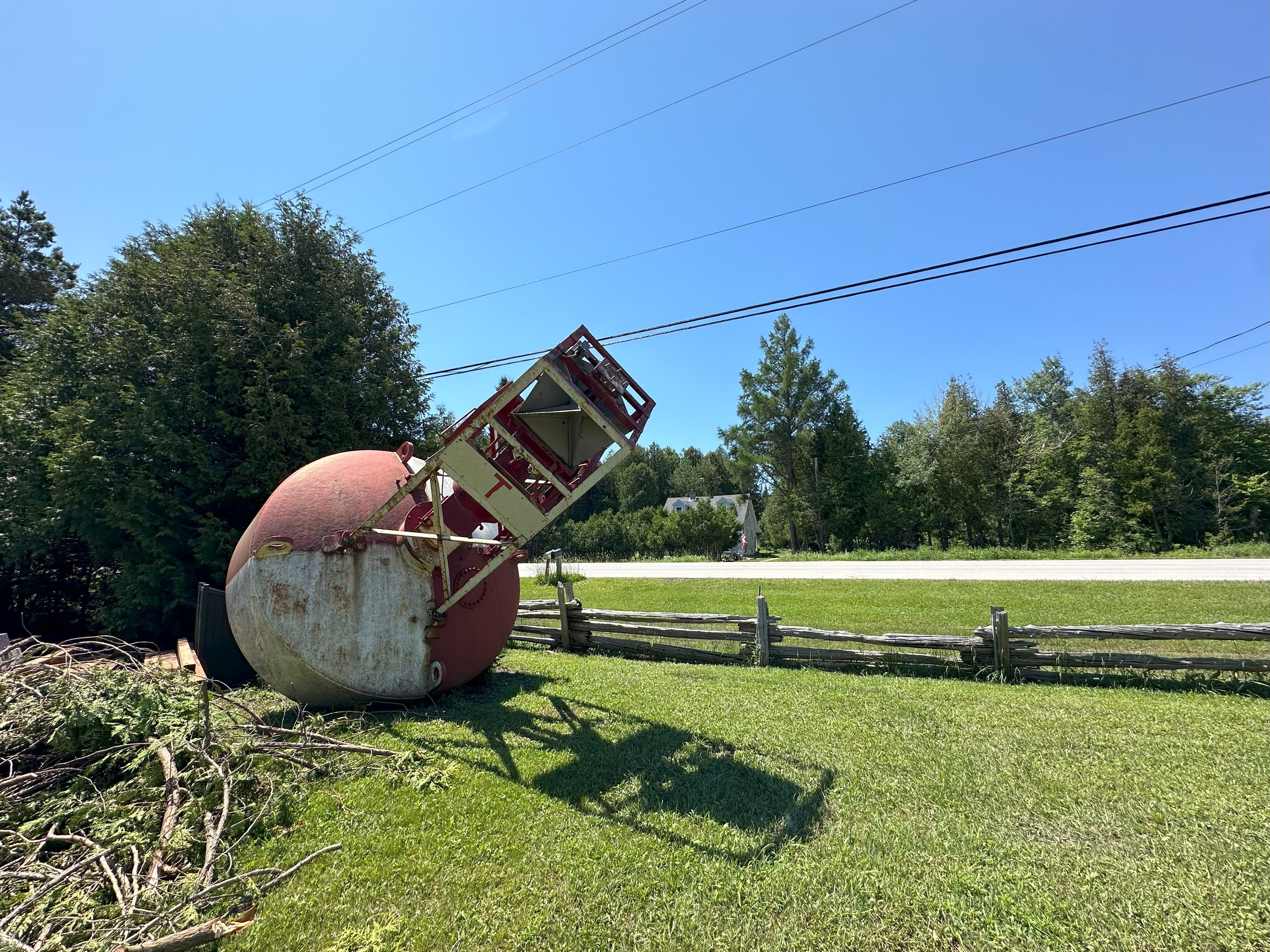 Outdoor photo of a large historical bouy displayed on a grassy field, with overhead wires and trees in the background.