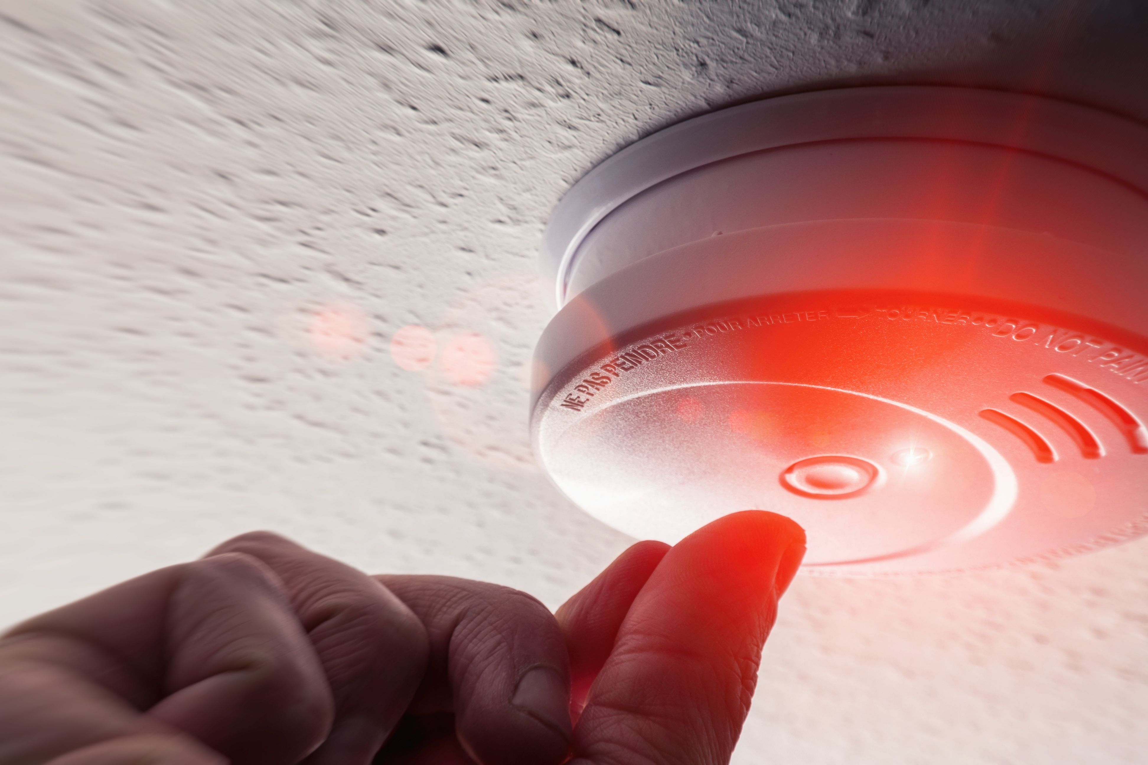 A hand push the smoke alarm button with a red light indicator showing.
