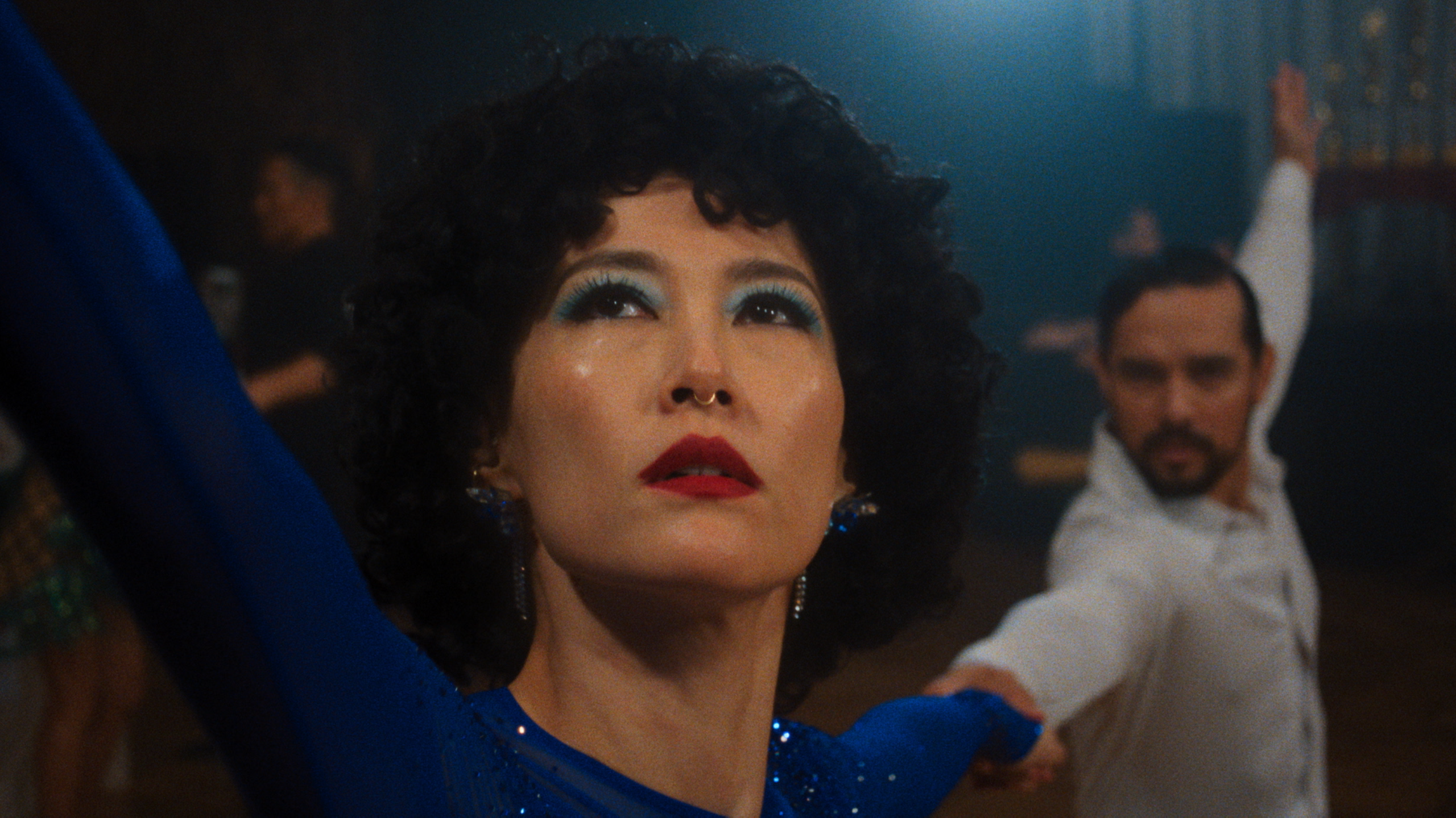 close up of a woman ballroom dancer with her dance partner in the background doing the Rumba