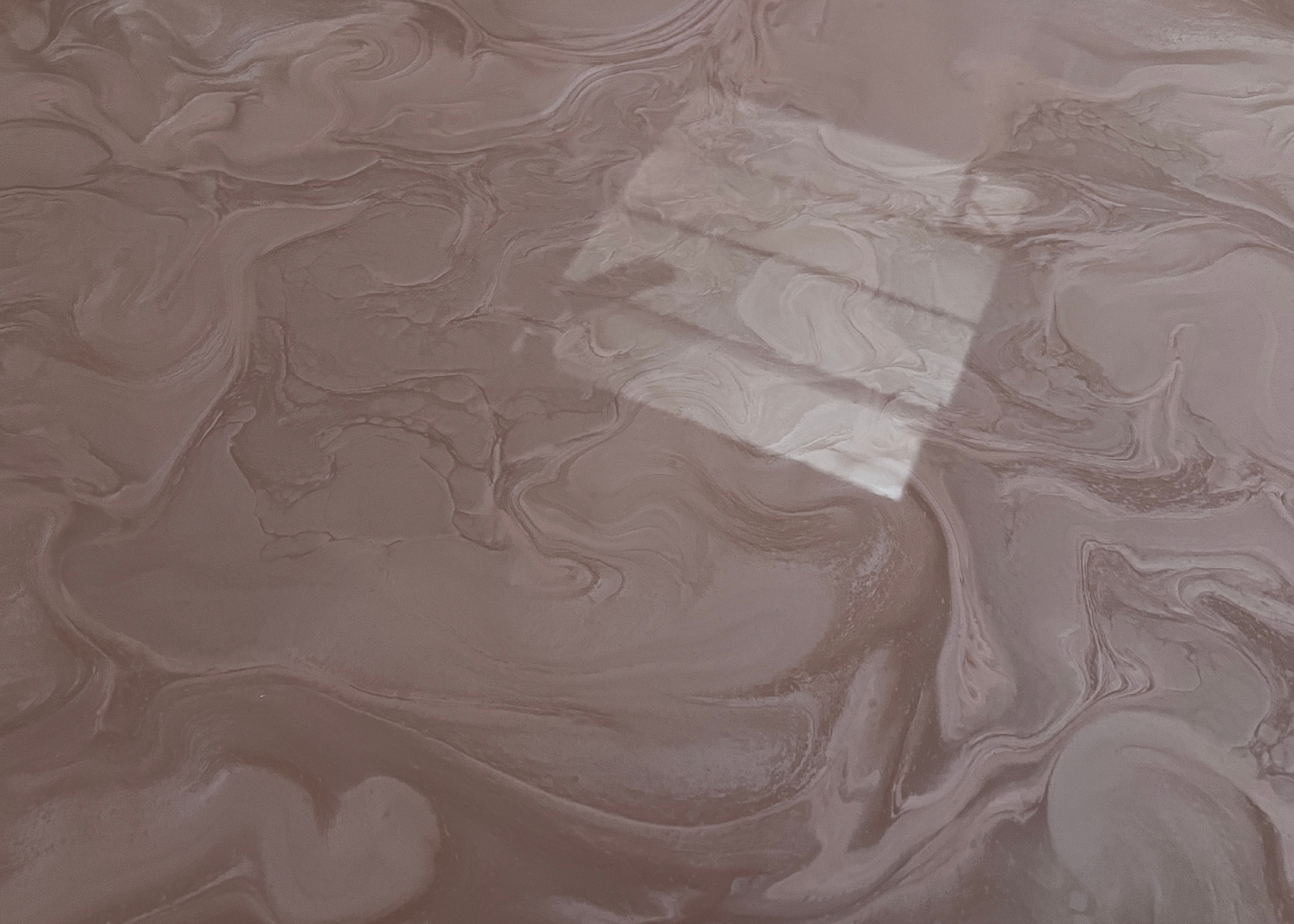 Close-up of a glossy marbled surface in muted brown, taupe, and cream tones, with swirling organic patterns and a bright rectangular reflection across the centre.