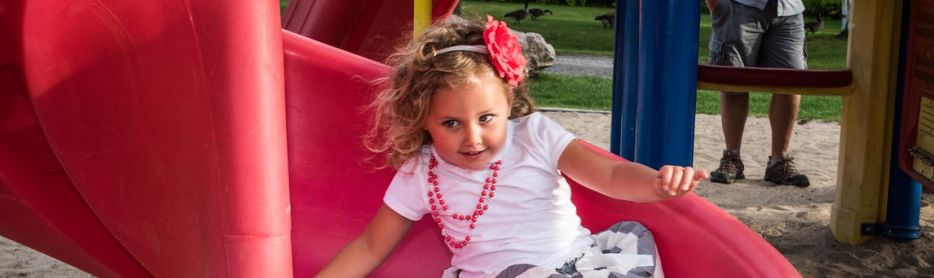 young girl sliding down a red slide at a playground