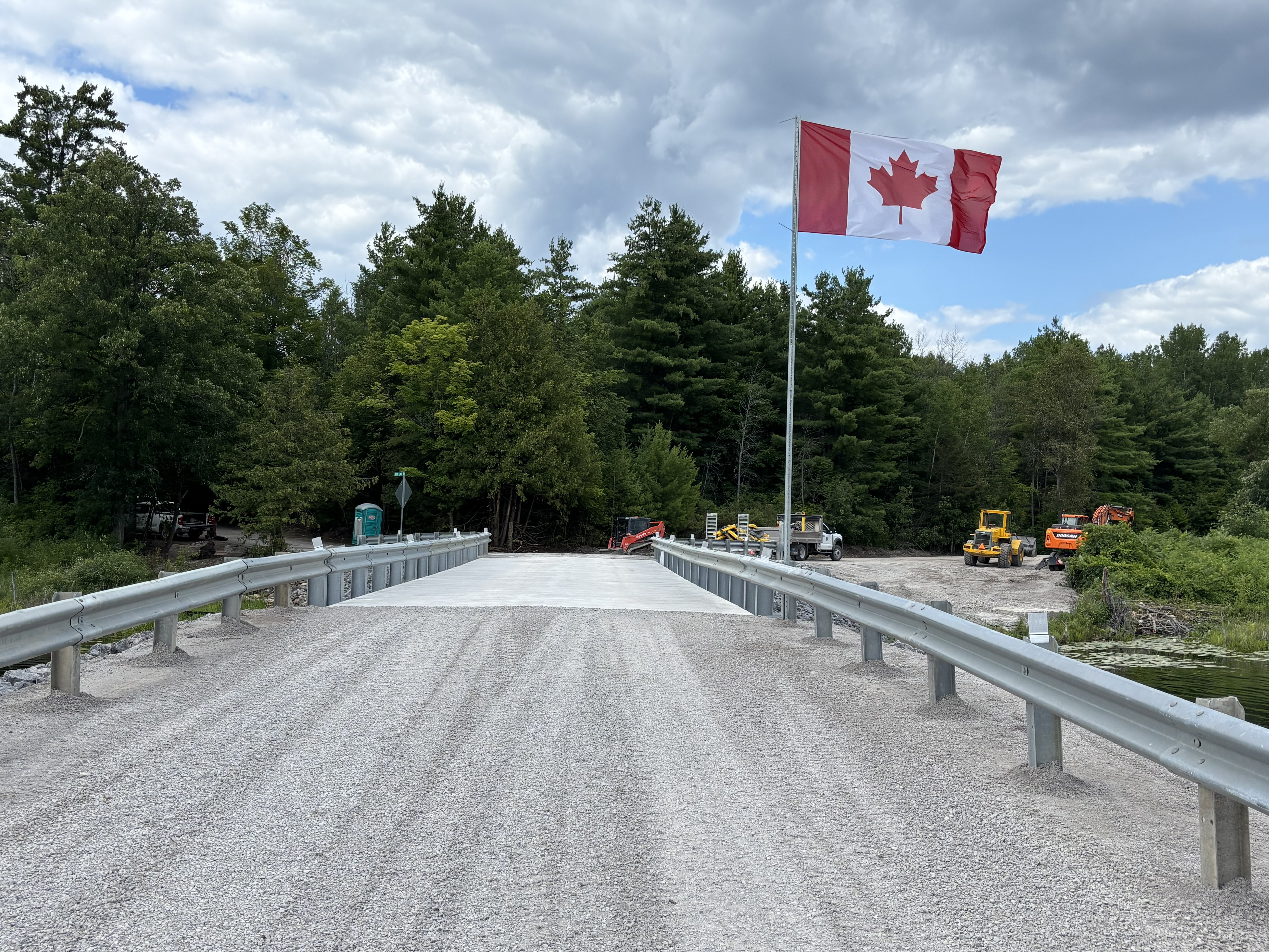 Gravel road leading to bridge with a Canadian flag flying